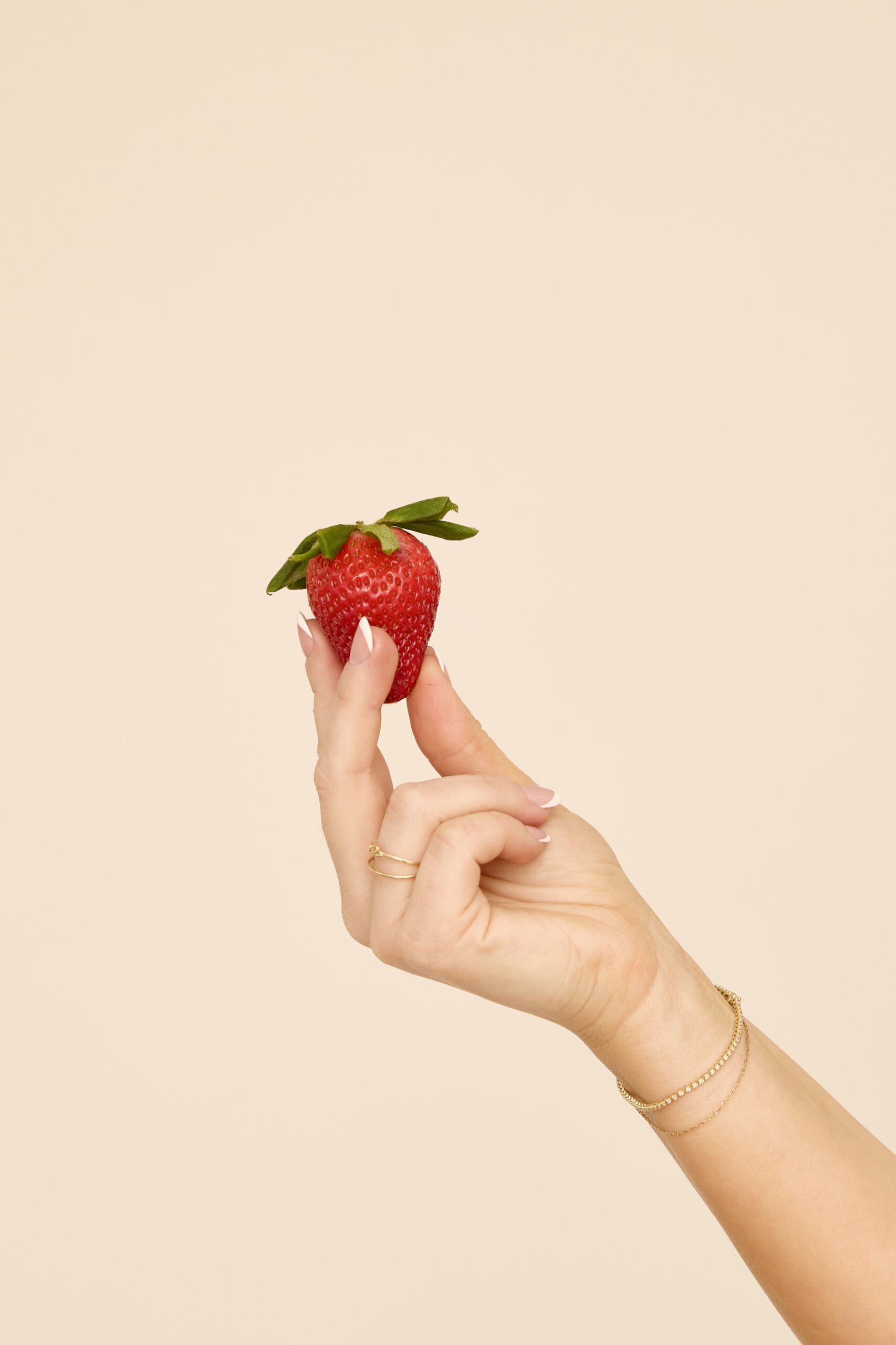 Hand holding a fresh strawberry, a nutrient-rich fruit that supports hormone balance and menstrual cycle health.