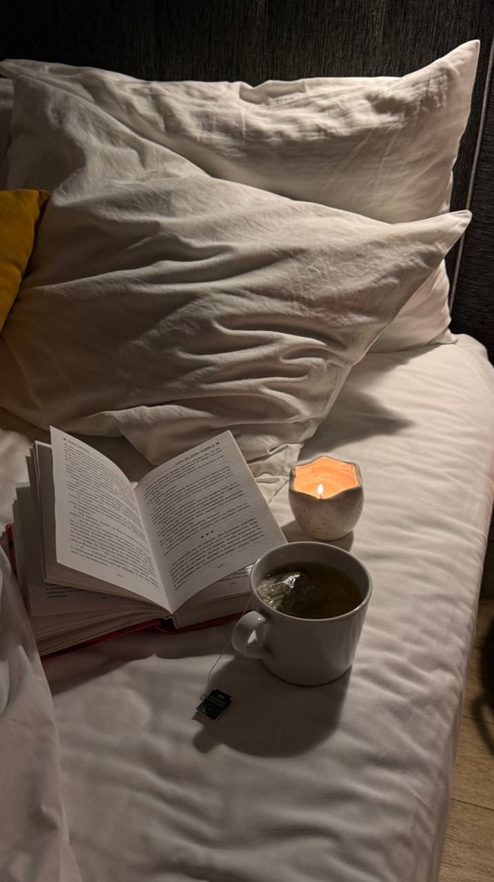 Cozy nighttime sleep hygiene setup with an open book, warm candlelight and a cup of tea on a neatly made bed.”