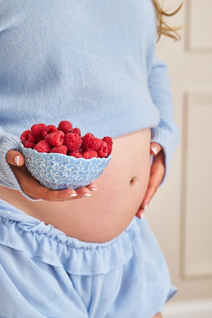 Pregnant dietitian Claire Rifkin holding kiwi and other fiber-rich foods for pregnancy constipation.